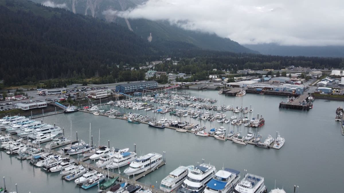 A small boat harbor full of fishing and pleasure boats beneath cloud-wrapped coastal mountains