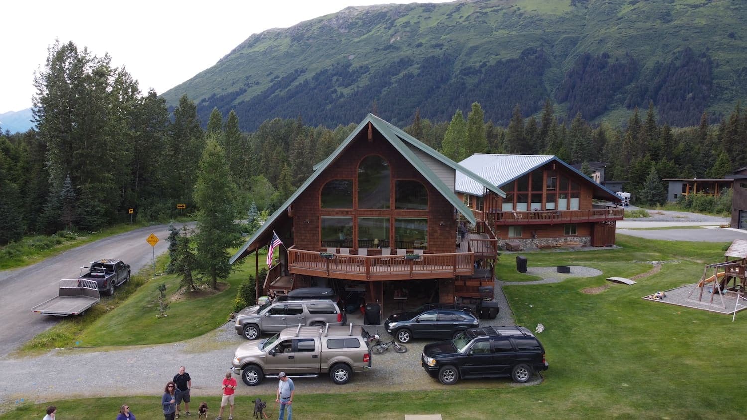 A luxury log home in Girdwood with a steep green roof set against forested mountains