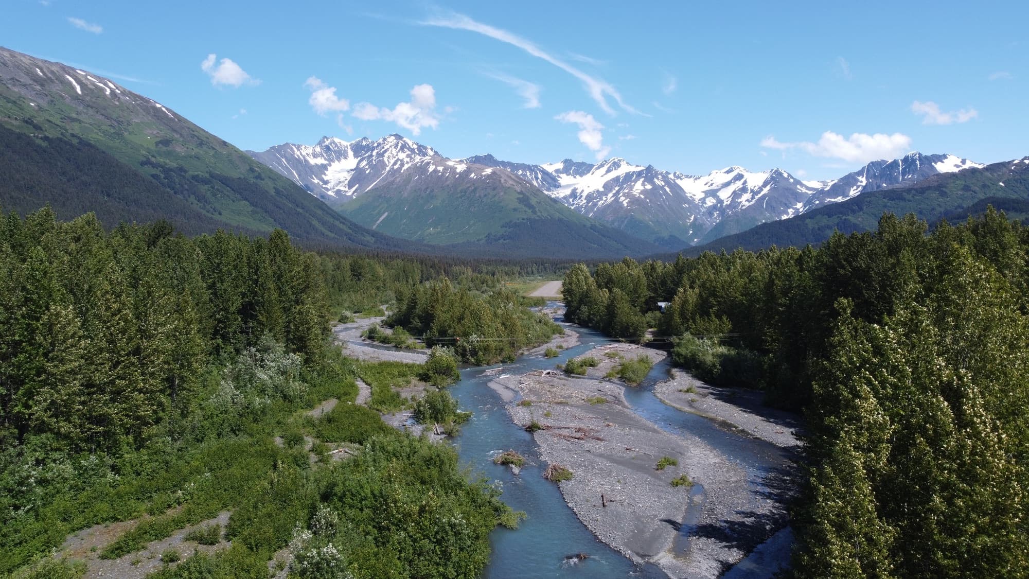 A glacial river winding through the forested valley below Girdwood's snow-capped peaks